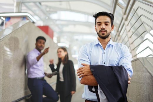 young executive standing with arms crossed is suspiciously, background are employee talking about him as bullying (resized)
